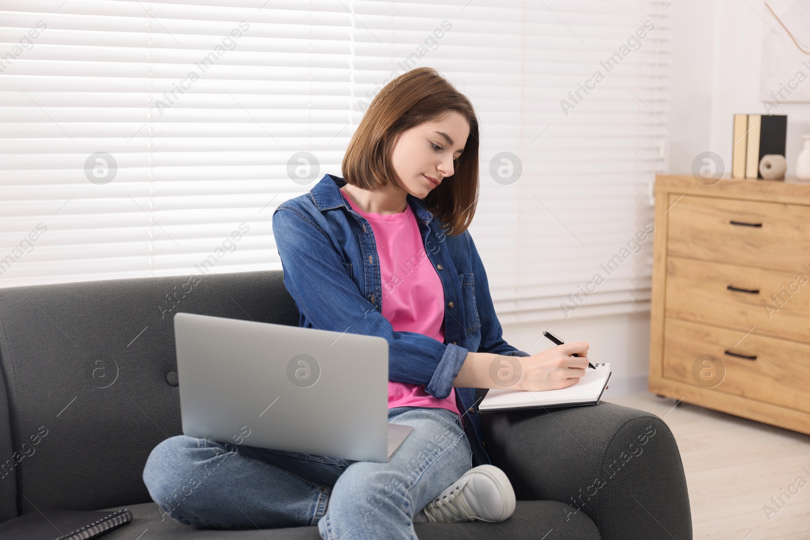 Photo of Teenager taking notes while working with laptop at home. Remote job