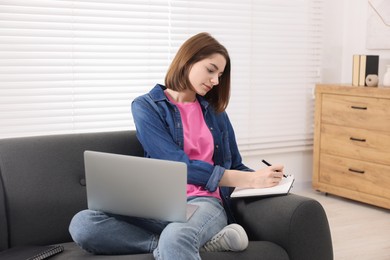 Teenager taking notes while working with laptop at home. Remote job