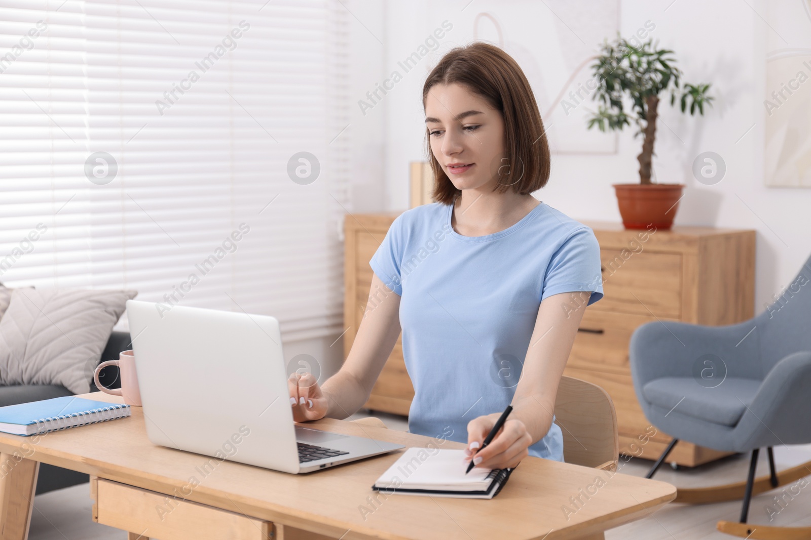 Photo of Teenager taking notes while working with laptop at home. Remote job