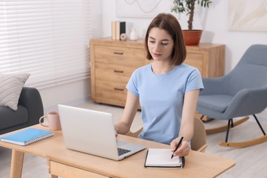 Teenager taking notes while working with laptop at home. Remote job