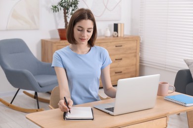 Teenager taking notes while working with laptop at home. Remote job