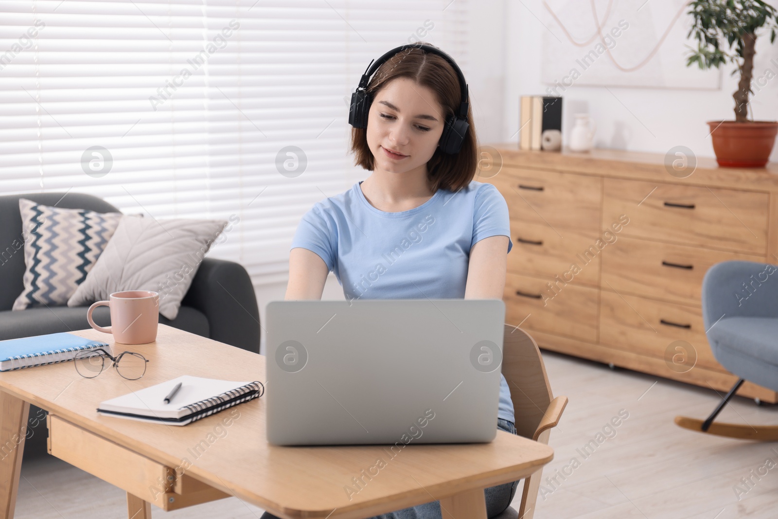 Photo of Teenager in headphones working with laptop at home. Remote job