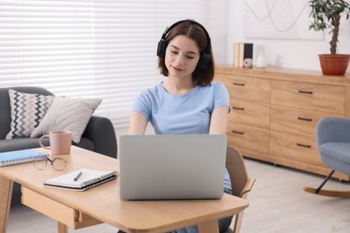 Teenager in headphones working with laptop at home. Remote job