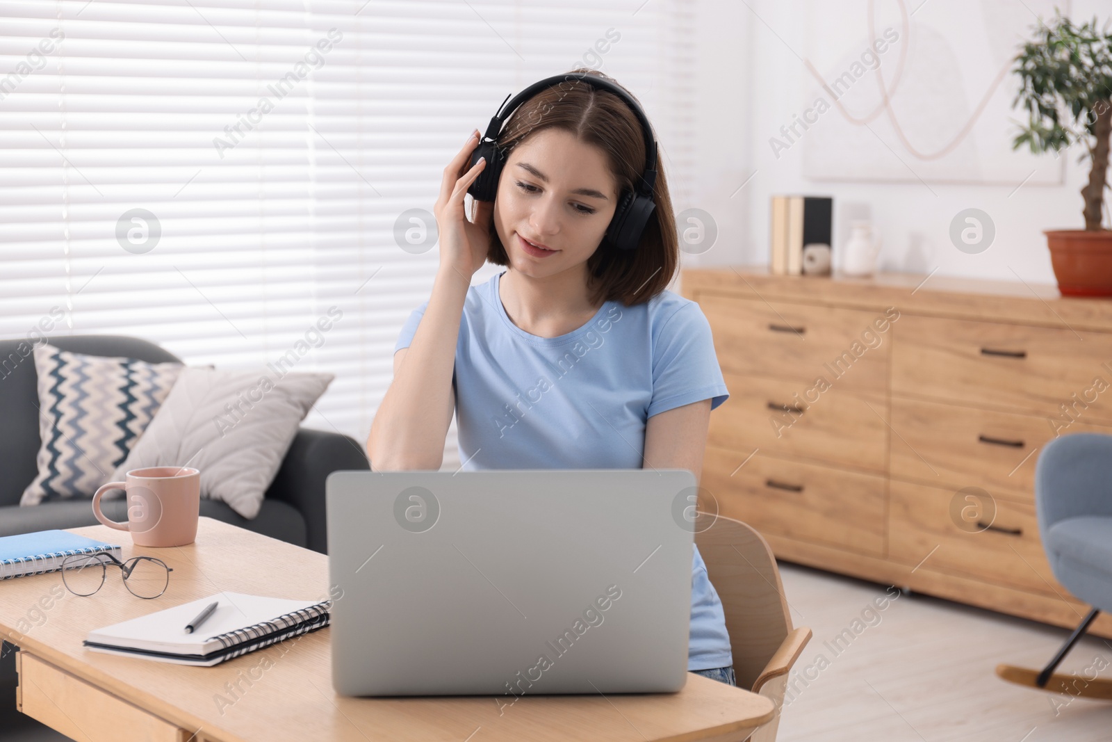 Photo of Teenager in headphones working with laptop at home. Remote job