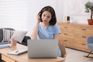 Teenager in headphones working with laptop at home. Remote job