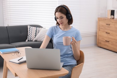 Teenager in headset with cup using laptop at home. Remote job