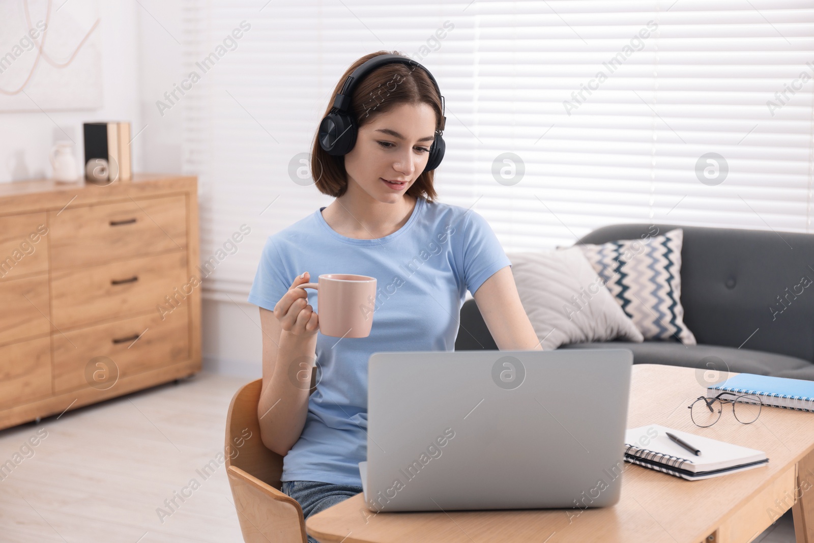 Photo of Teenager in headset with cup using laptop at home. Remote job