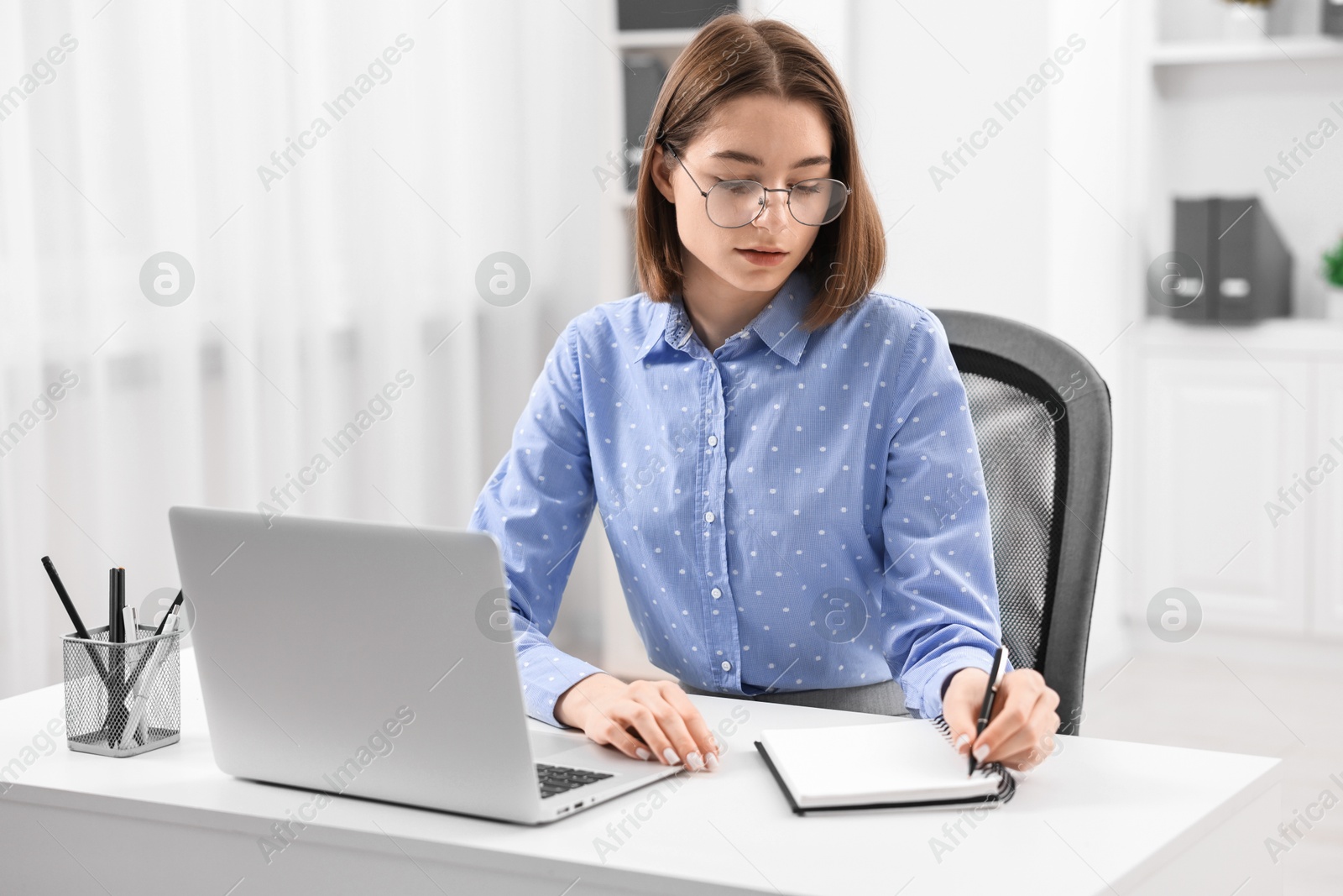 Photo of Teenager taking notes while working with laptop at home. Remote job