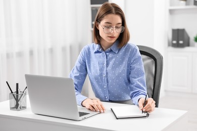 Teenager taking notes while working with laptop at home. Remote job