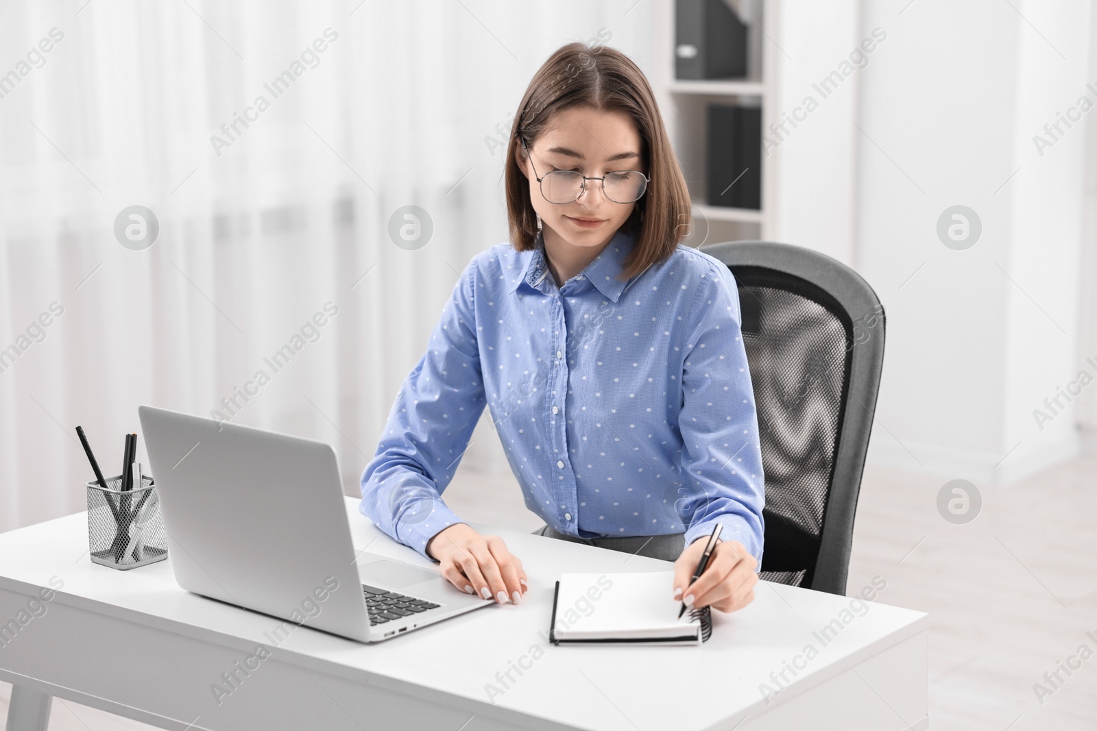 Photo of Teenager taking notes while working with laptop at home. Remote job