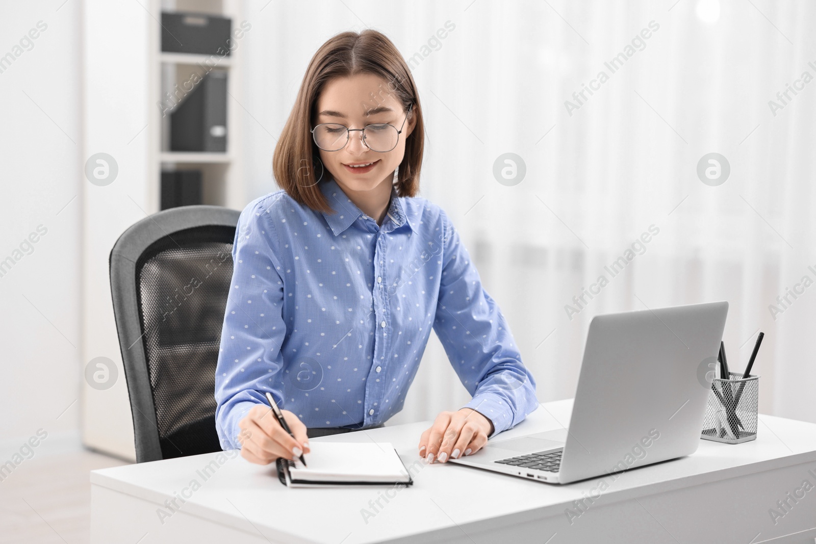 Photo of Teenager taking notes while working with laptop at home. Remote job