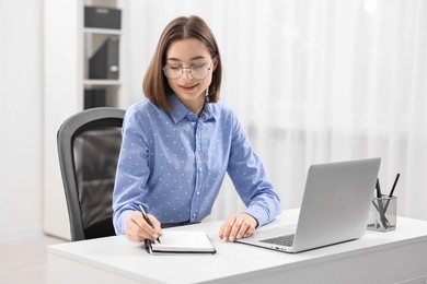 Teenager taking notes while working with laptop at home. Remote job