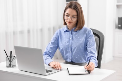 Teenager taking notes while working with laptop at home. Remote job