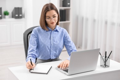 Teenager taking notes while working with laptop at home. Remote job