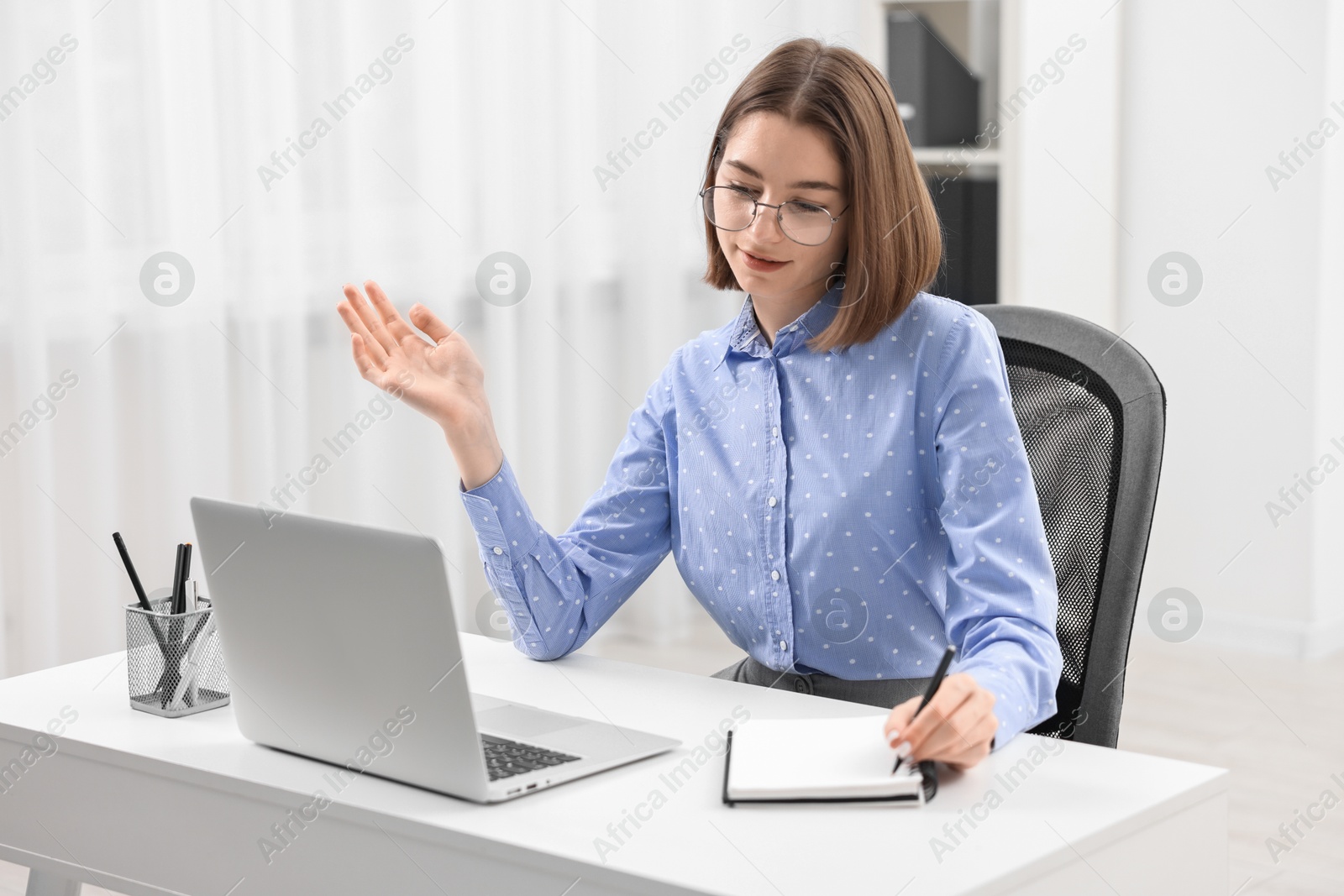 Photo of Teenager taking notes while working with laptop at home. Remote job