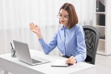 Teenager taking notes while working with laptop at home. Remote job