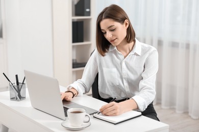 Teenager taking notes while working with laptop at home. Remote job