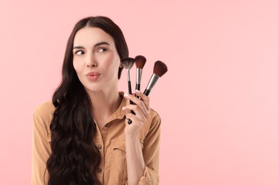 Photo of Attractive woman with beautiful makeup holding brushes on pink background. Space for text