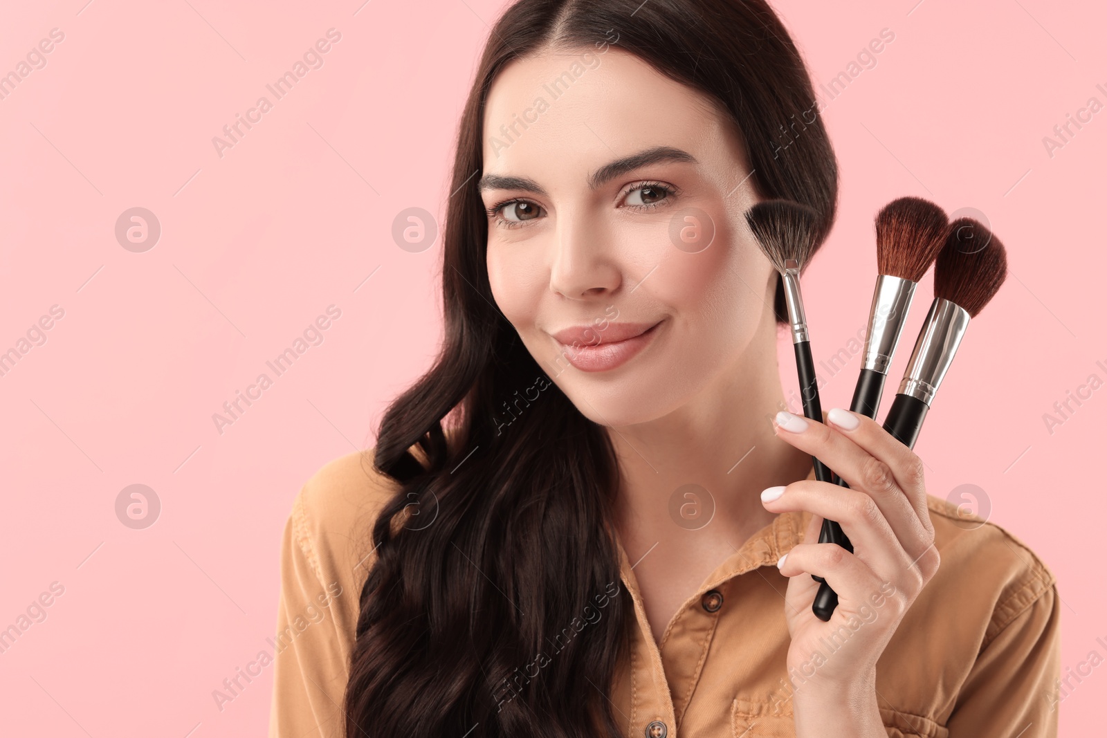 Photo of Attractive woman with beautiful makeup holding brushes on pink background