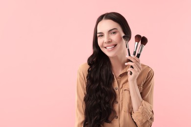 Photo of Beautiful makeup. Smiling woman with brushes on pink background, space for text