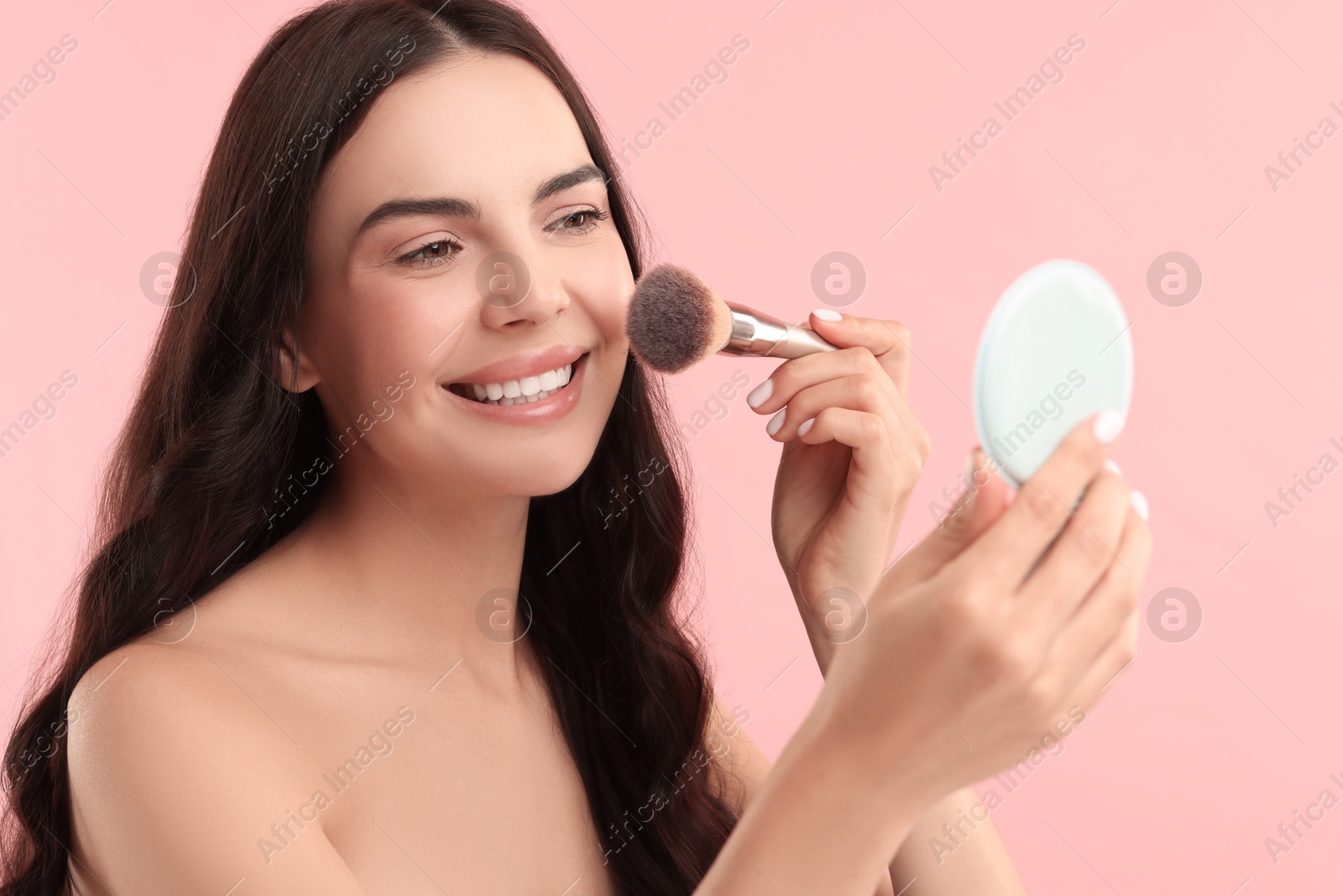 Photo of Beautiful makeup. Smiling woman applying blush with brush on pink background