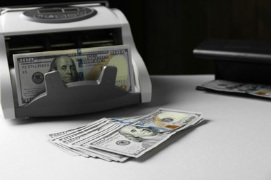 Photo of Dollar banknotes and money counter machine on light table, closeup