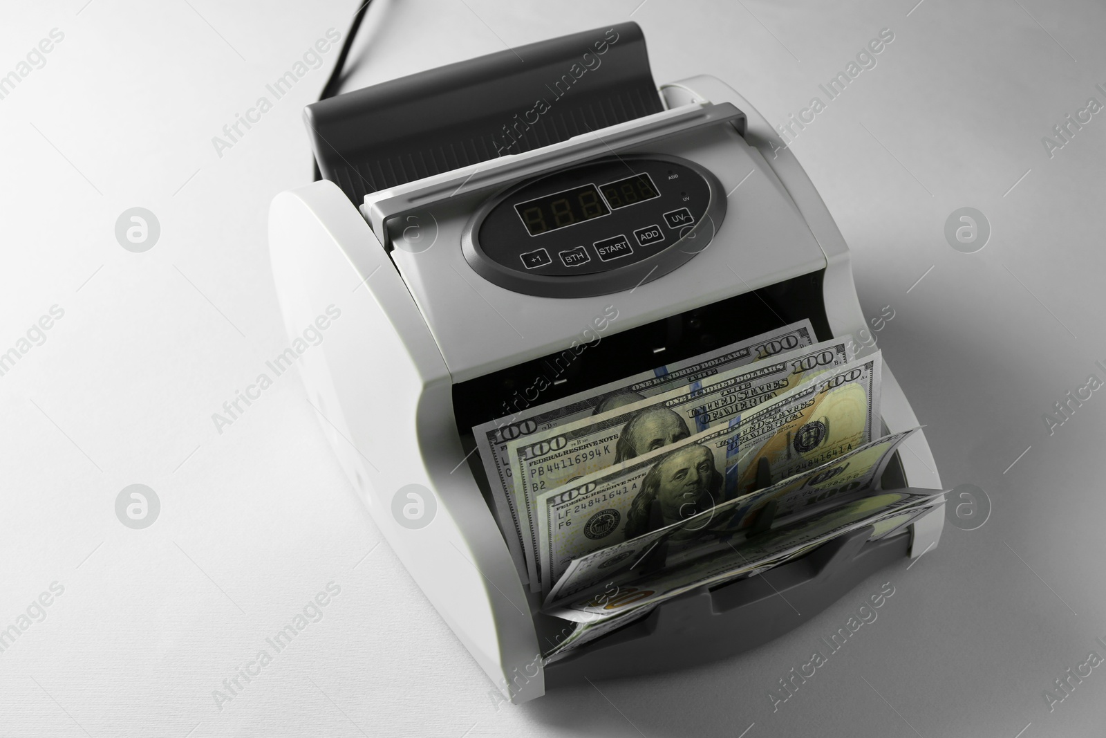 Photo of Money counter machine with dollar banknotes on light table, above view