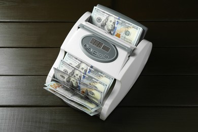 Photo of Money counter machine with dollar banknotes on wooden table