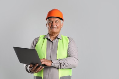 Engineer in hard hat with laptop on grey background, space for text