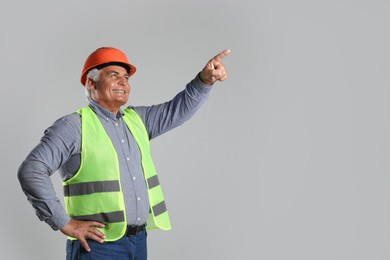 Engineer in hard hat pointing at something on grey background, space for text