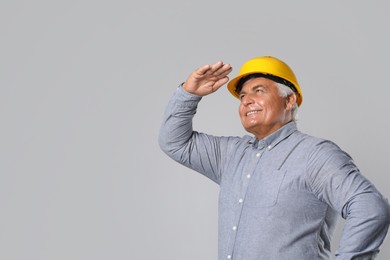 Engineer in hard hat on grey background, space for text