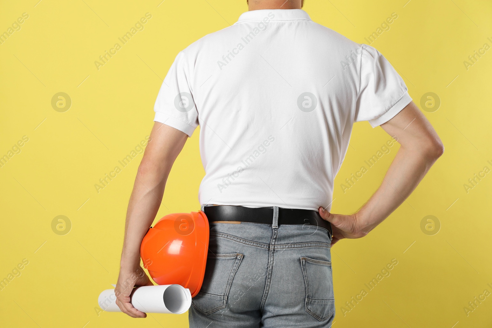 Photo of Engineer with hard hat and draft on yellow background, back view