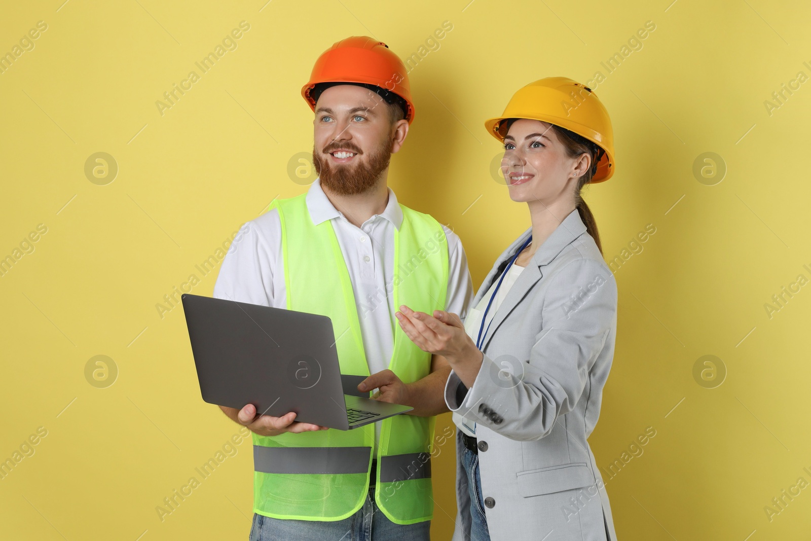 Photo of Engineers in hard hats with laptop on yellow background