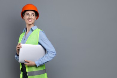 Engineer in hard hat with laptop on grey background, space for text