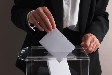 Photo of Woman putting her vote into ballot box at table against grey background, closeup