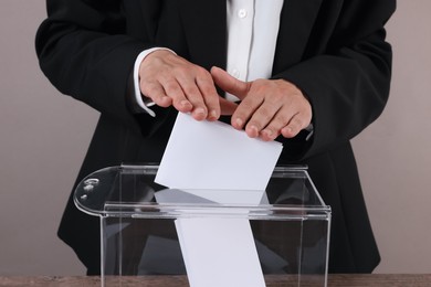 Photo of Woman putting her vote into ballot box at table against grey background, closeup