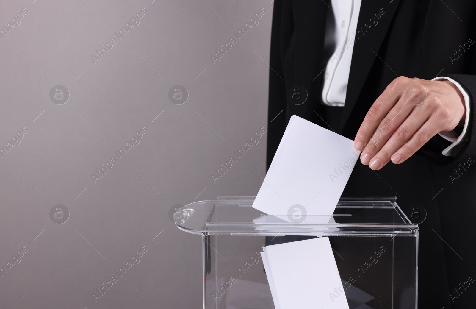 Photo of Woman putting her vote into ballot box against grey background, closeup. Space for text