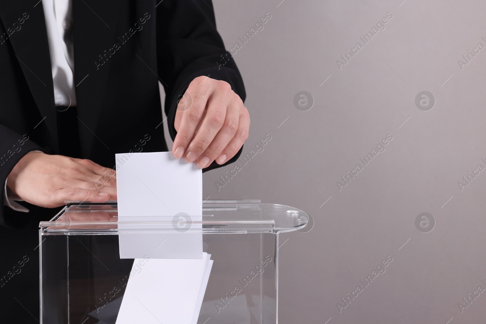 Photo of Woman putting her vote into ballot box against grey background, closeup. Space for text