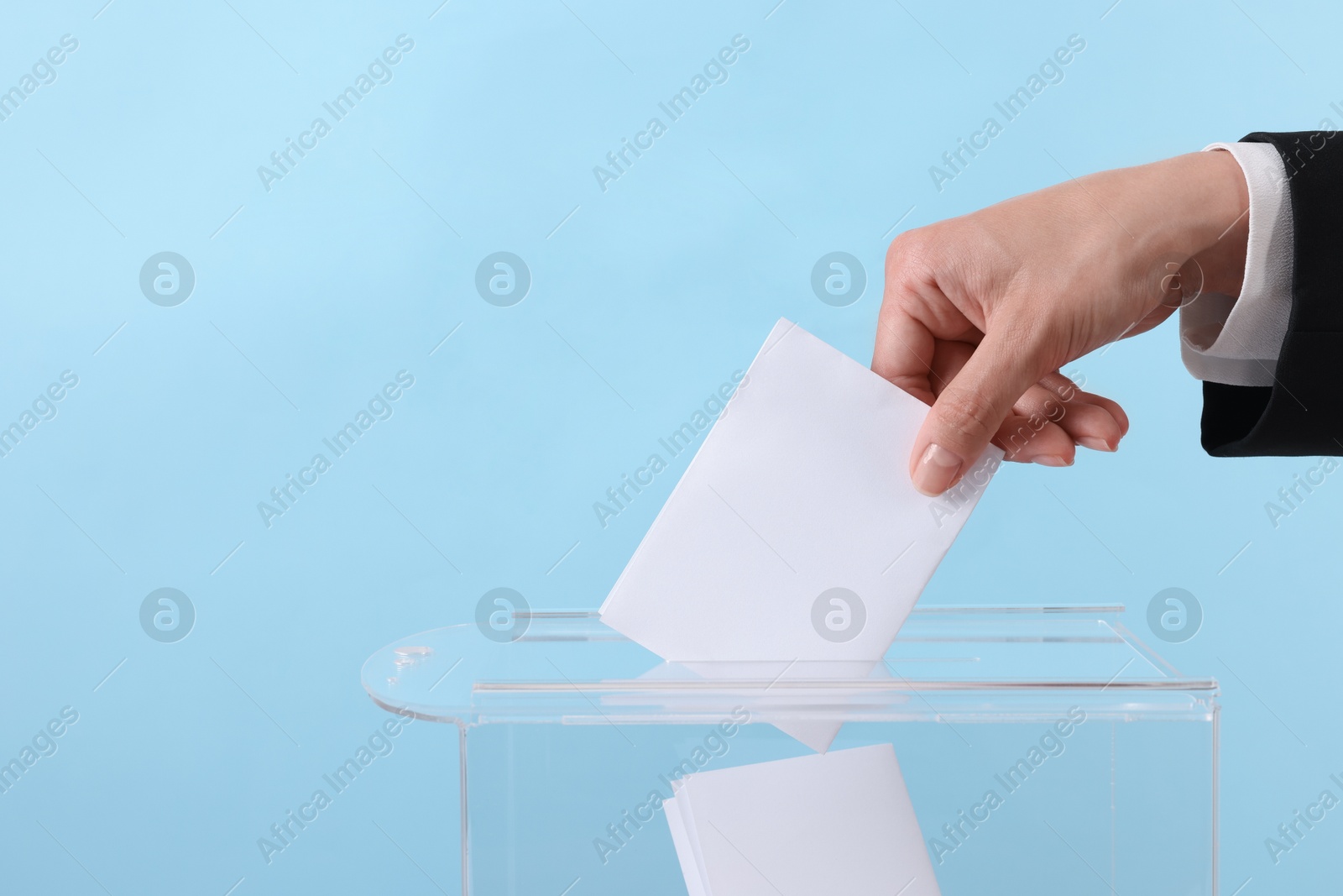 Photo of Woman putting her vote into ballot box against light blue background, closeup. Space for text