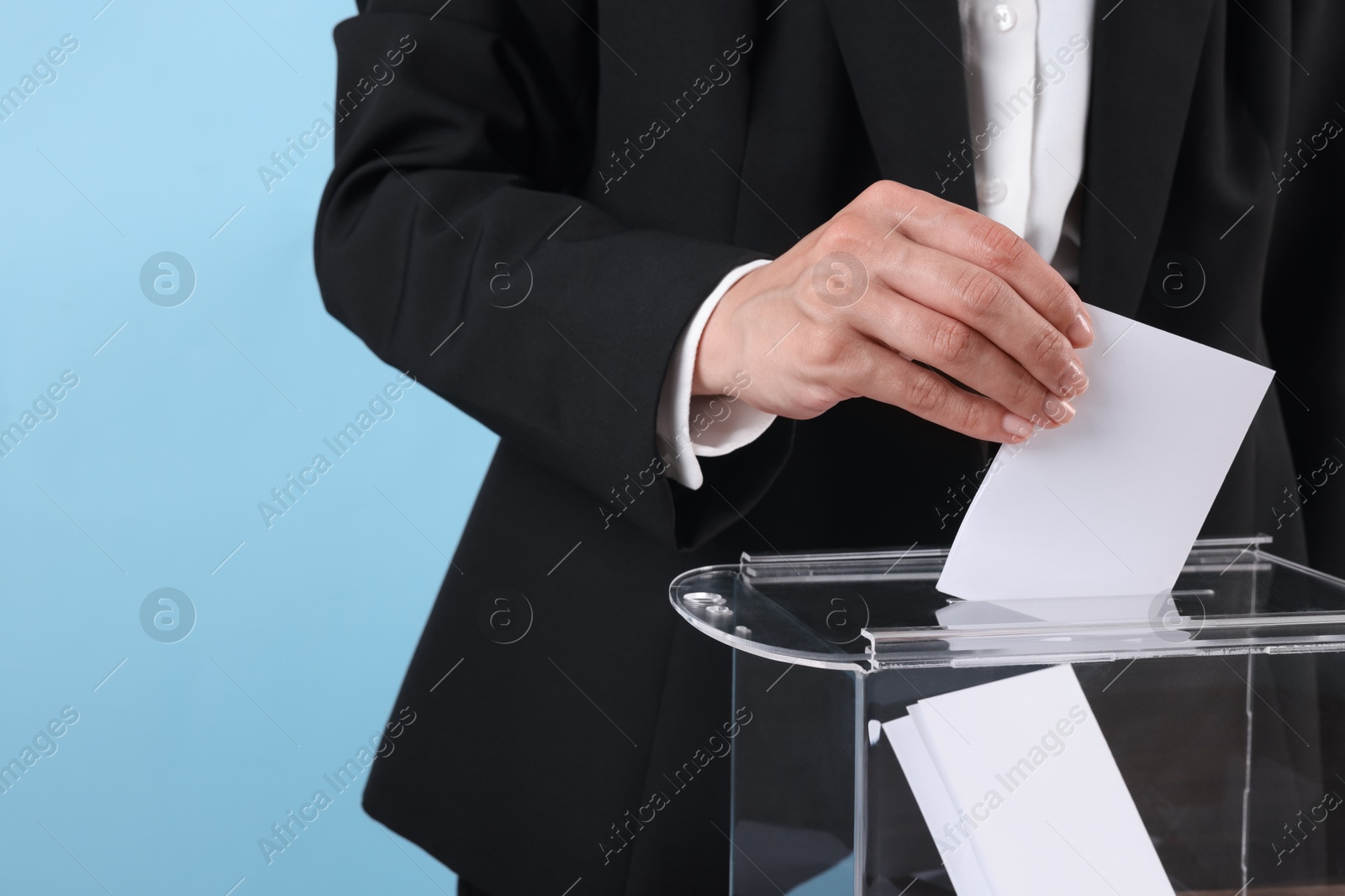 Photo of Woman putting her vote into ballot box against light blue background, closeup