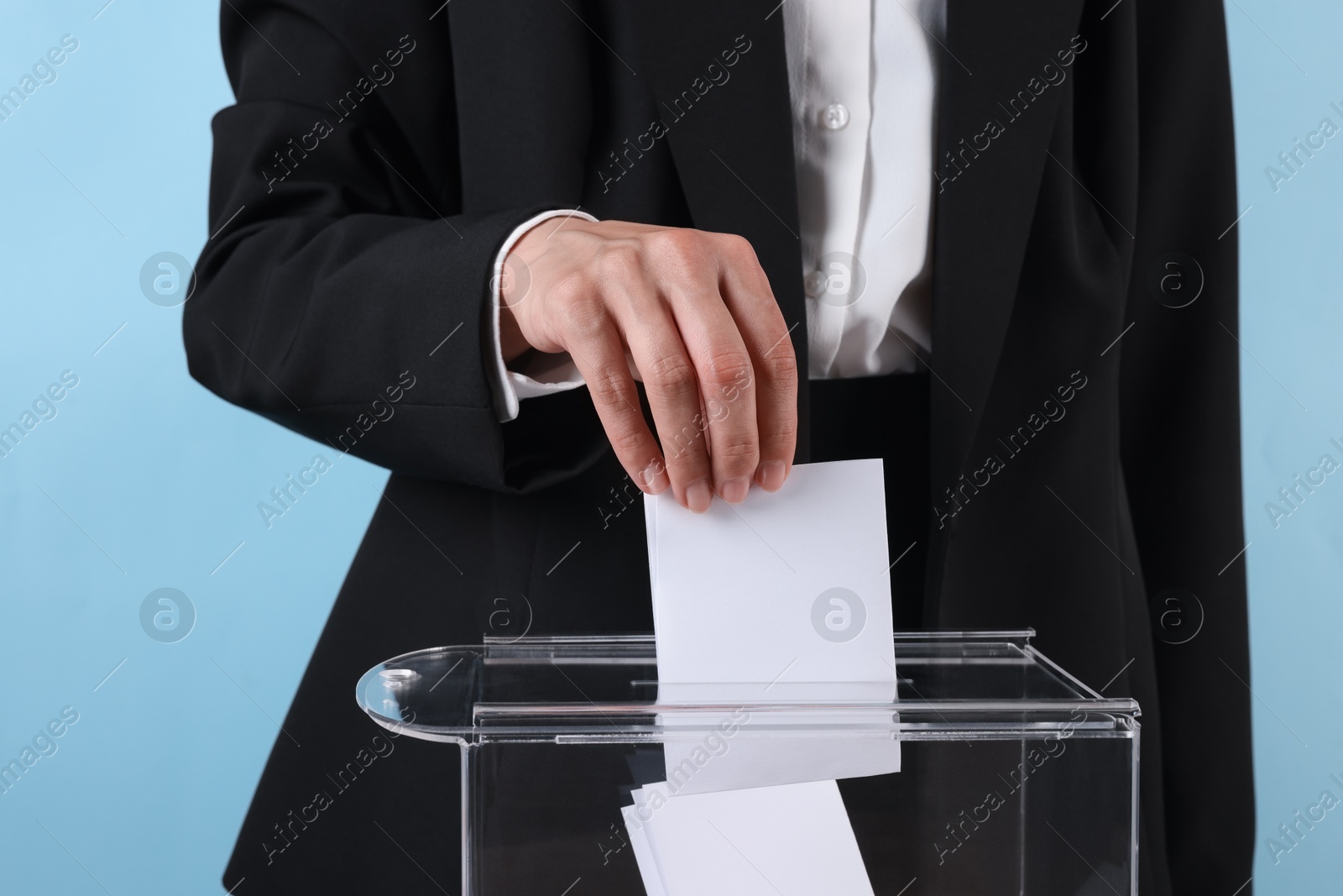 Photo of Woman putting her vote into ballot box against light blue background, closeup