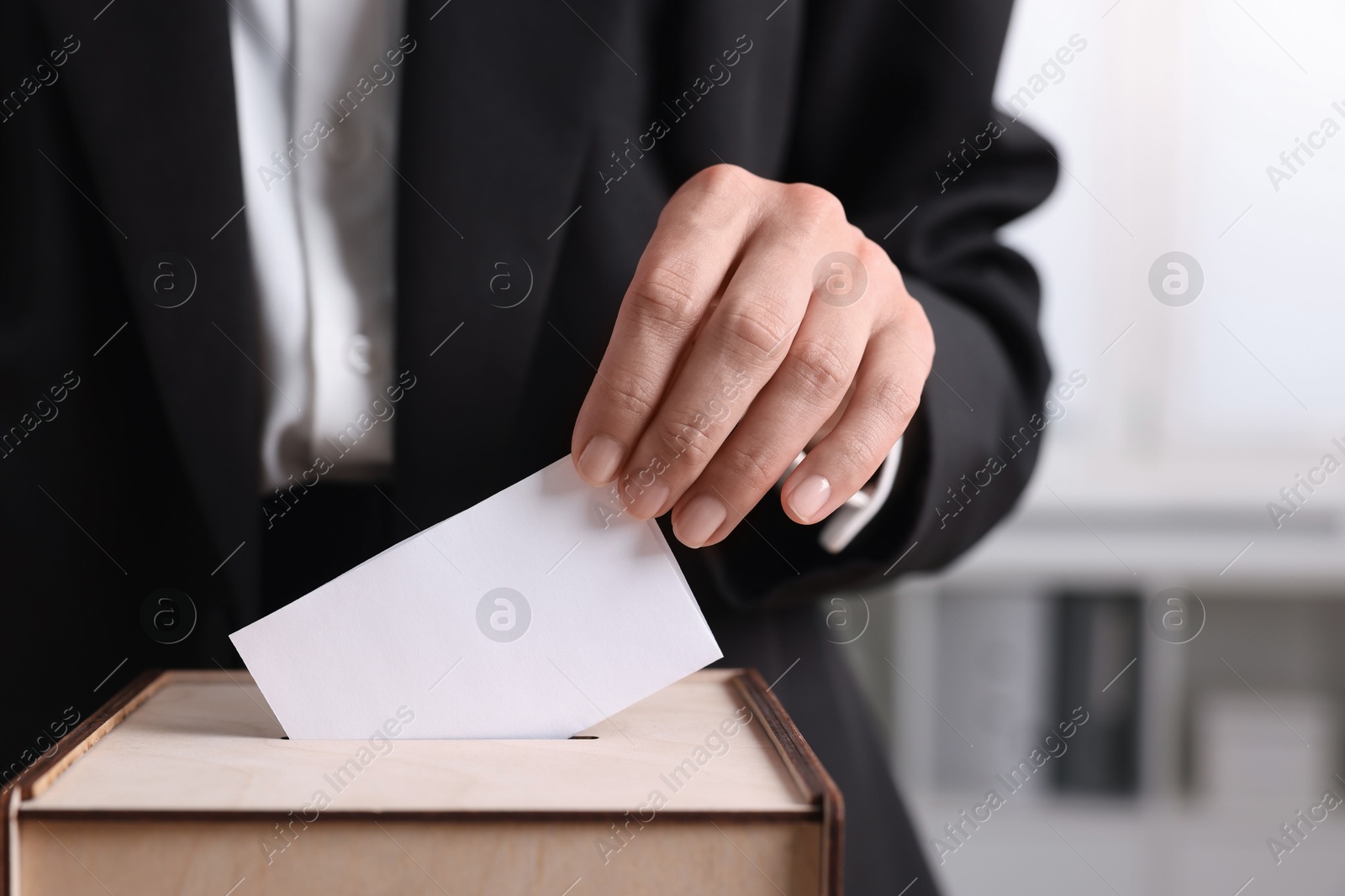 Photo of Woman putting her vote into ballot box indoors, closeup