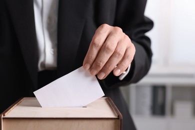 Photo of Woman putting her vote into ballot box indoors, closeup