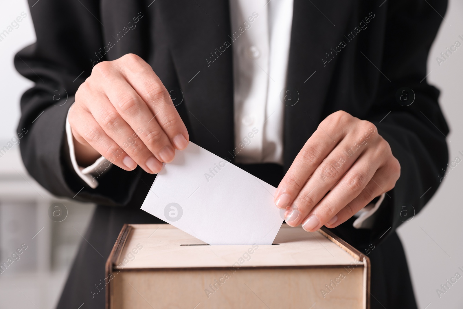 Photo of Woman putting her vote into ballot box indoors, closeup