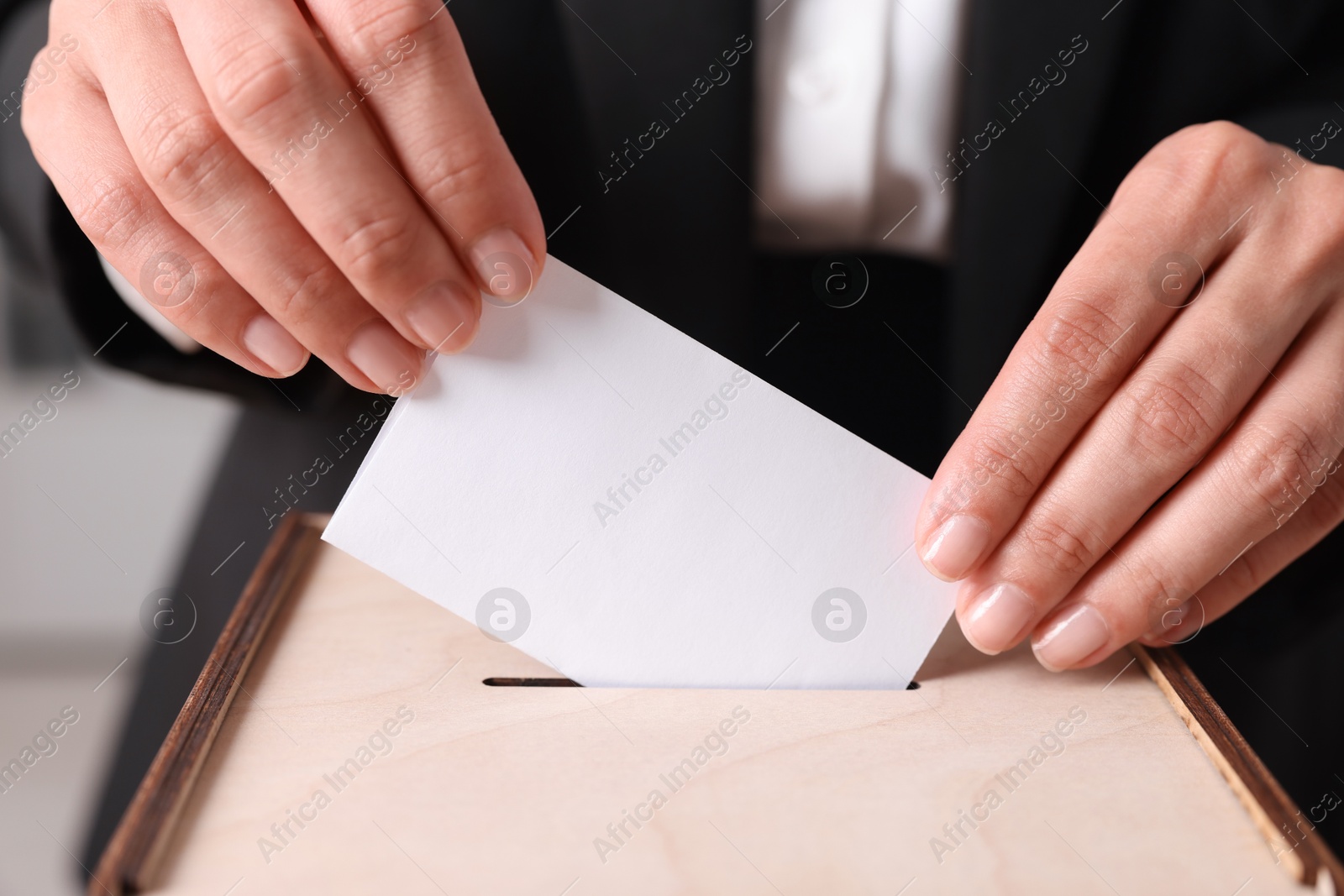 Photo of Woman putting her vote into ballot box indoors, closeup