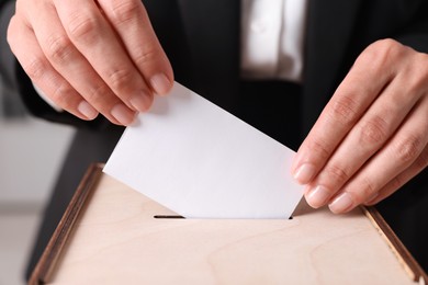 Photo of Woman putting her vote into ballot box indoors, closeup