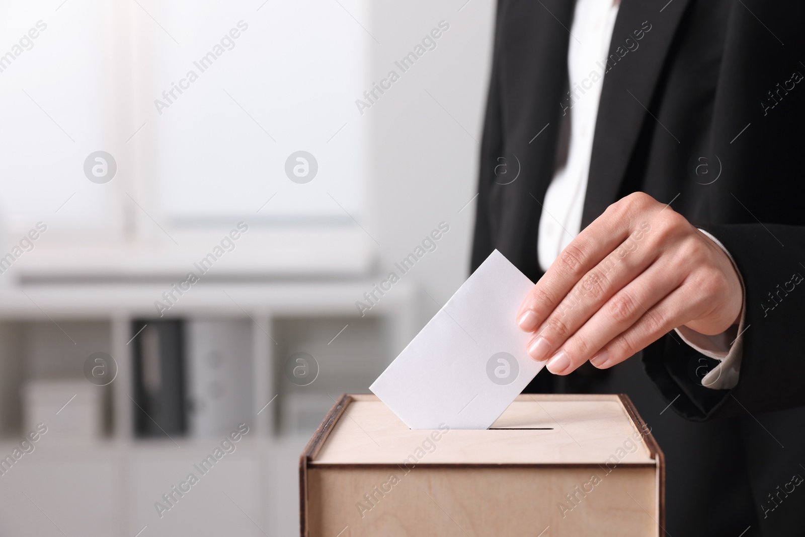 Photo of Woman putting her vote into ballot box indoors, closeup. Space for text