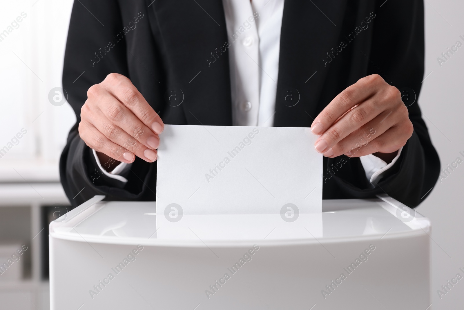 Photo of Woman putting her vote into ballot box indoors, closeup