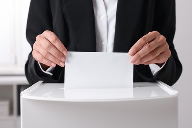 Photo of Woman putting her vote into ballot box indoors, closeup