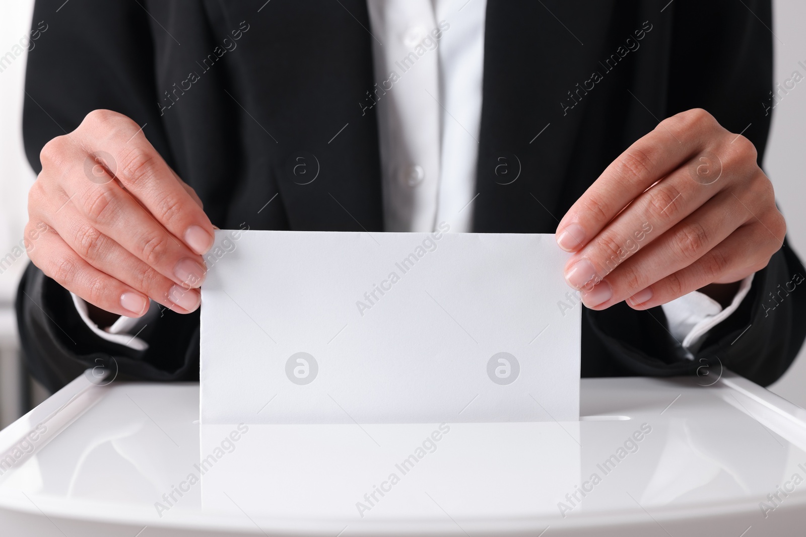 Photo of Woman putting her vote into ballot box indoors, closeup